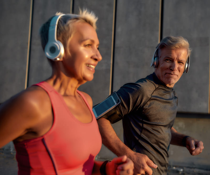  Sporty and happy middle-aged couple in headphones running together through the city street in the morning.