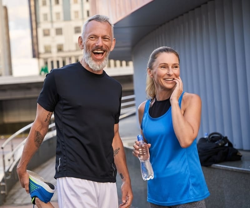 Portrait of happy sportive middle aged couple, man and woman in sportswear smiling, standing together outdoors ready for workout